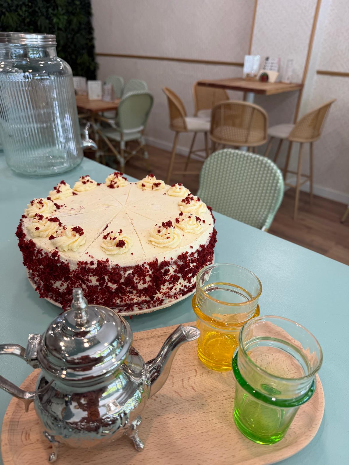 Interior de Mediterránea Café en el Actur de Zaragoza con mesas de madera, sillas de ratán y tarta red velvet en barra
